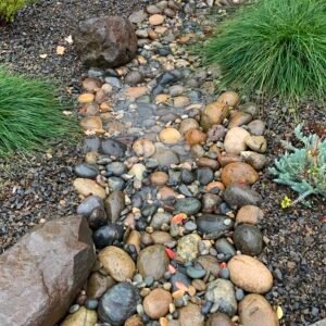 A human made creekbed of smooth round stones in shades of gray & brown, filled with rainwater.