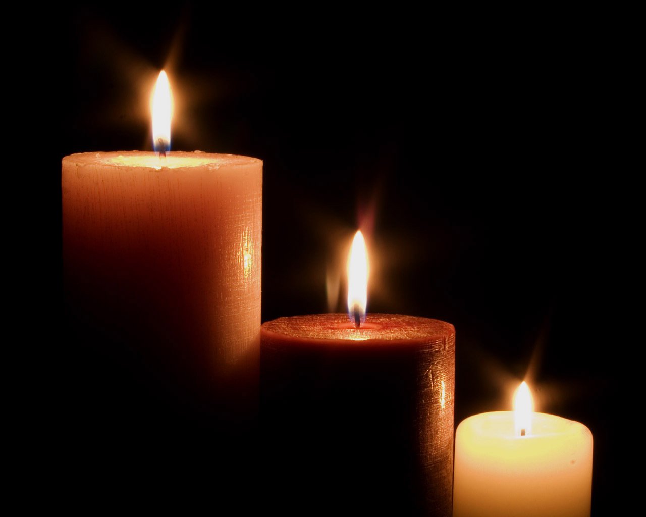 three lit candles of different heights glowing against a completely black background