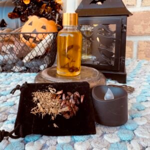 glass small bottle with herb floating in gold liquid sitting on top a brass stand. a black led light in front. a black cloth with herbs sitting on it is propped up against the brass stand. witchy halloween decorations in the back ground. all sitting on top a light blue and white towel.