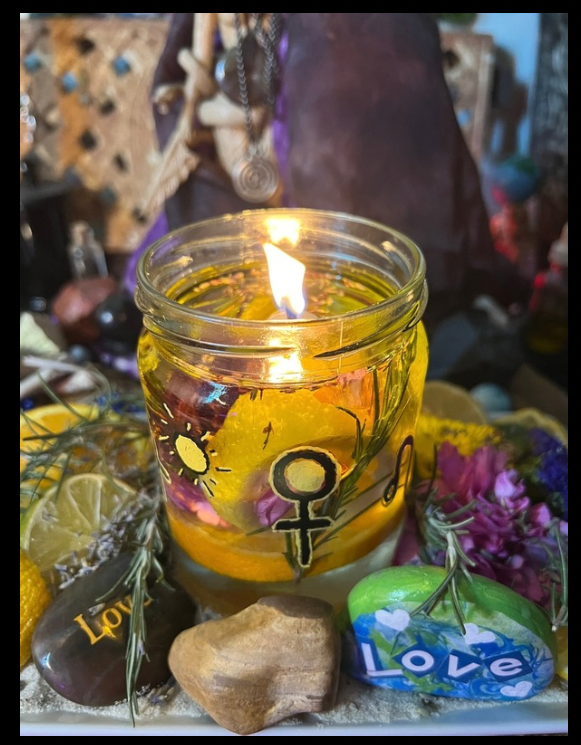 a glass jar with yellow liquid and a flame in the middle. the jar has a venus symbol and various rocks surrounding it